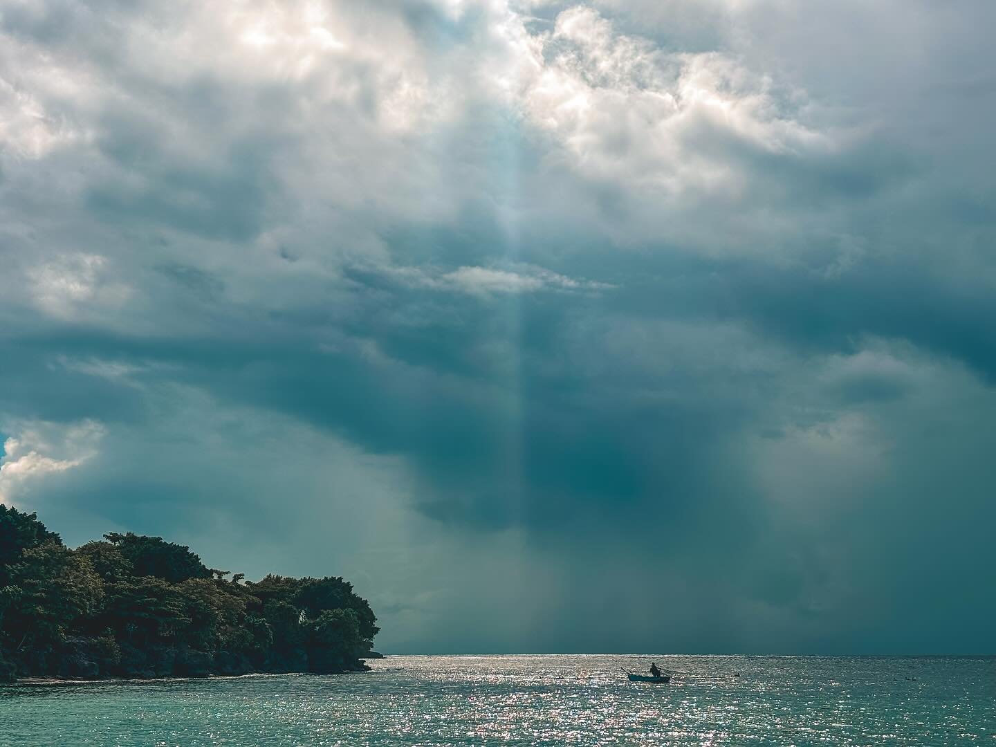 A boat on calm ocean waters near a tree-covered coastline under a cloudy sky.