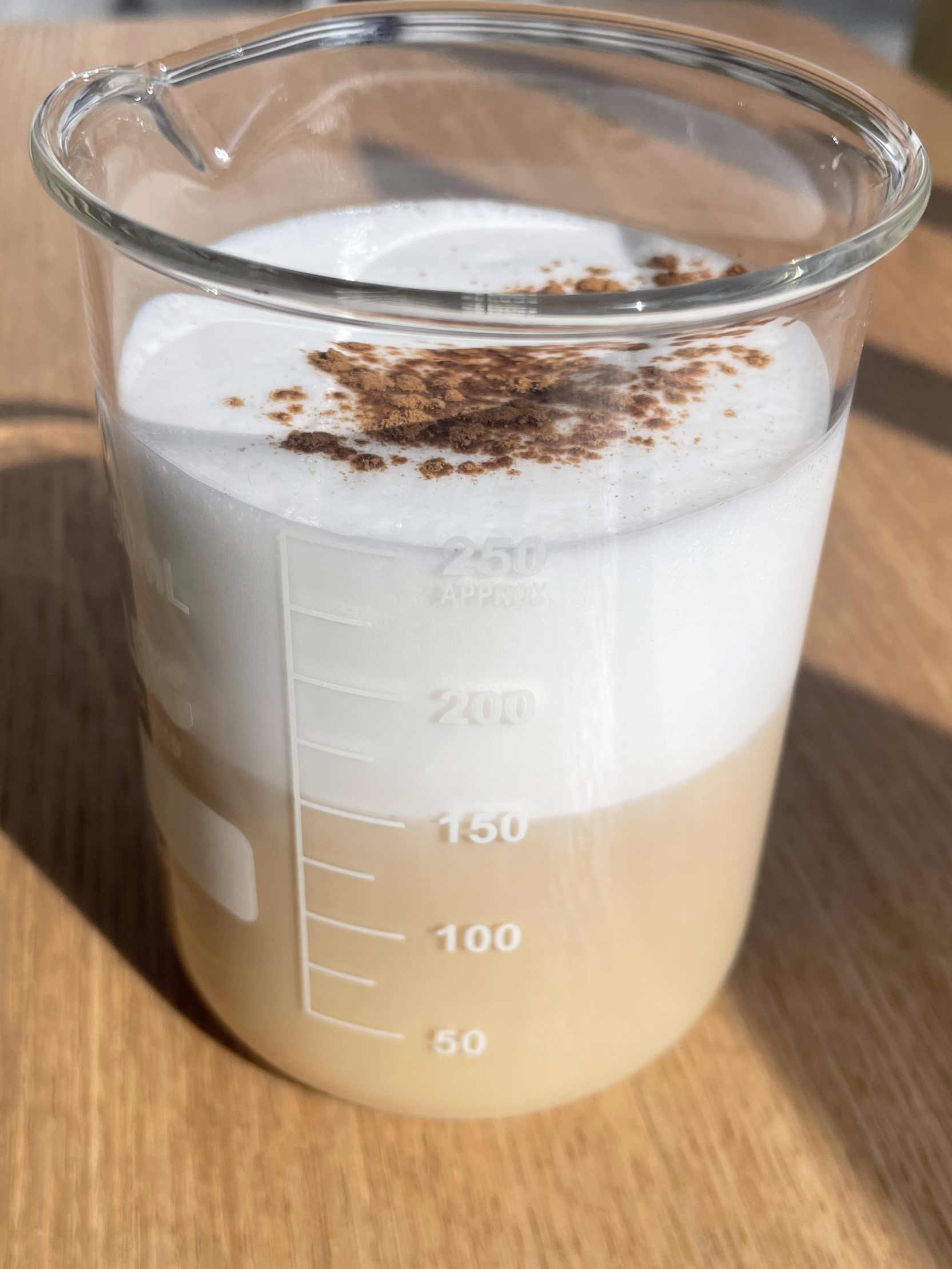 Cappuccino servido en vaso de laboratorio con espuma de leche y cacao en polvo, en Explora Family Café Madrid