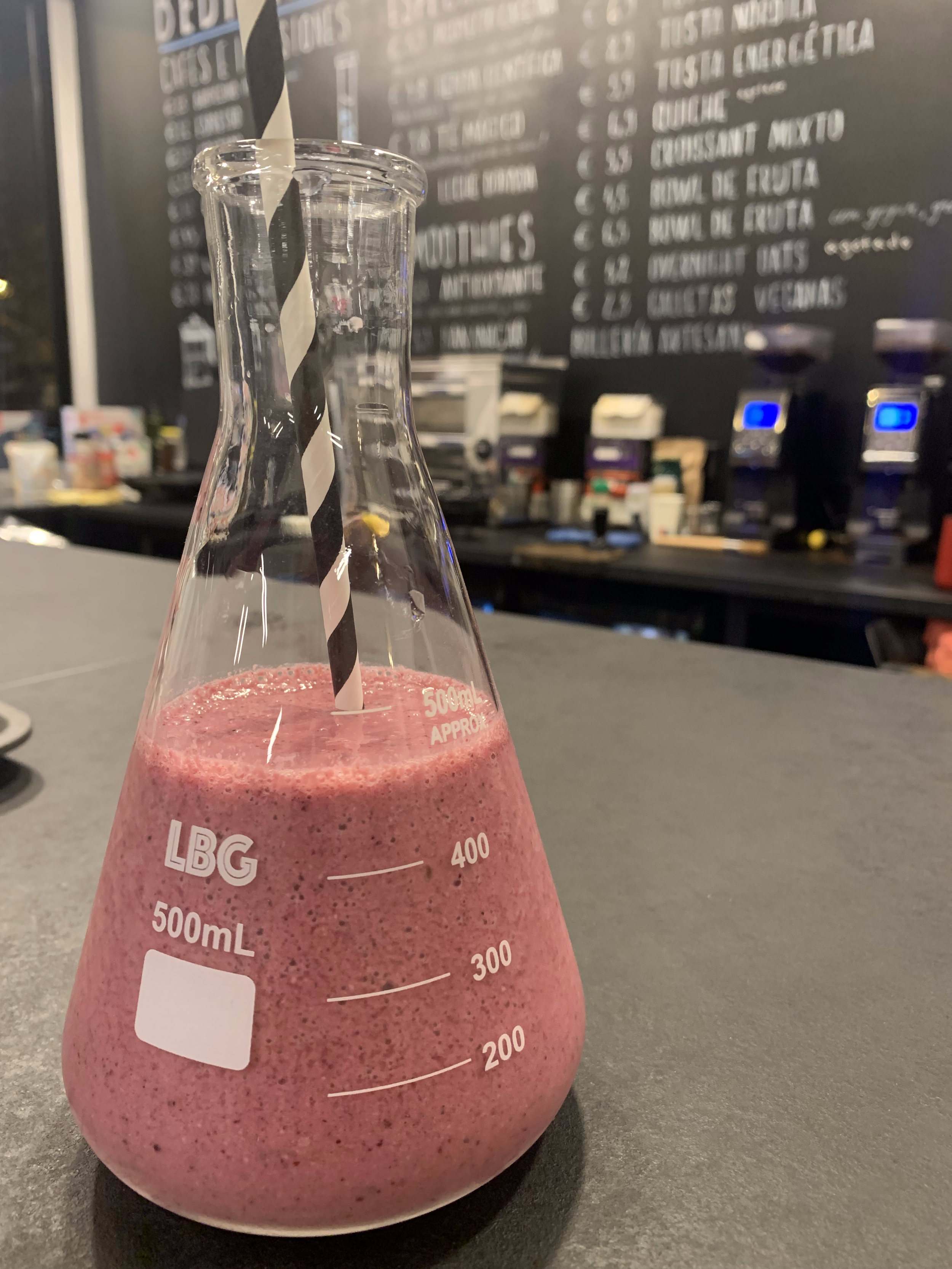Batido antioxidante de frutos rojos, coco y banana servido en matraz de laboratorio en Explora Family Café Madrid