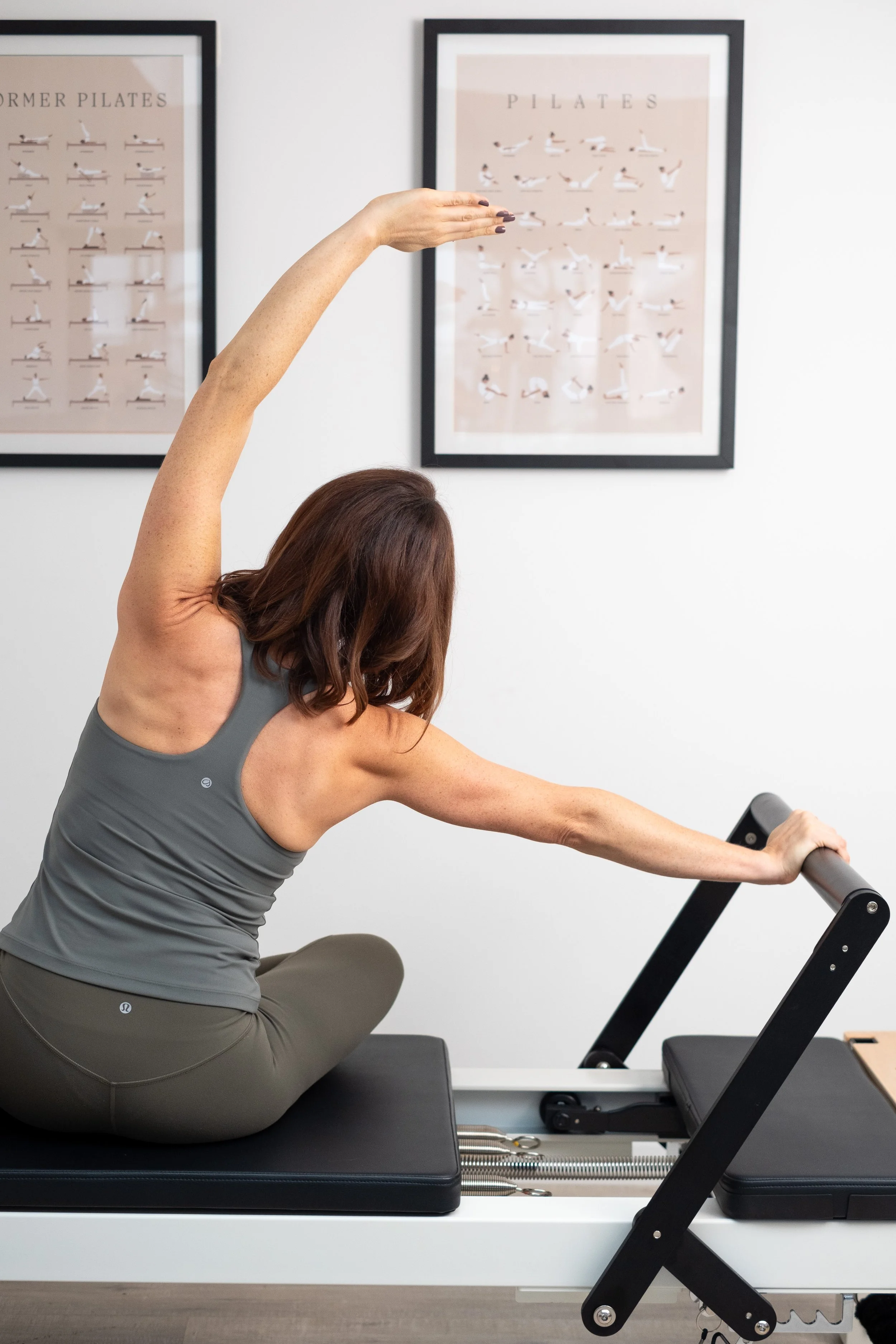 Woman doing Pilates exercise on reformer machine in fitness studio with Pilates posters on wall.