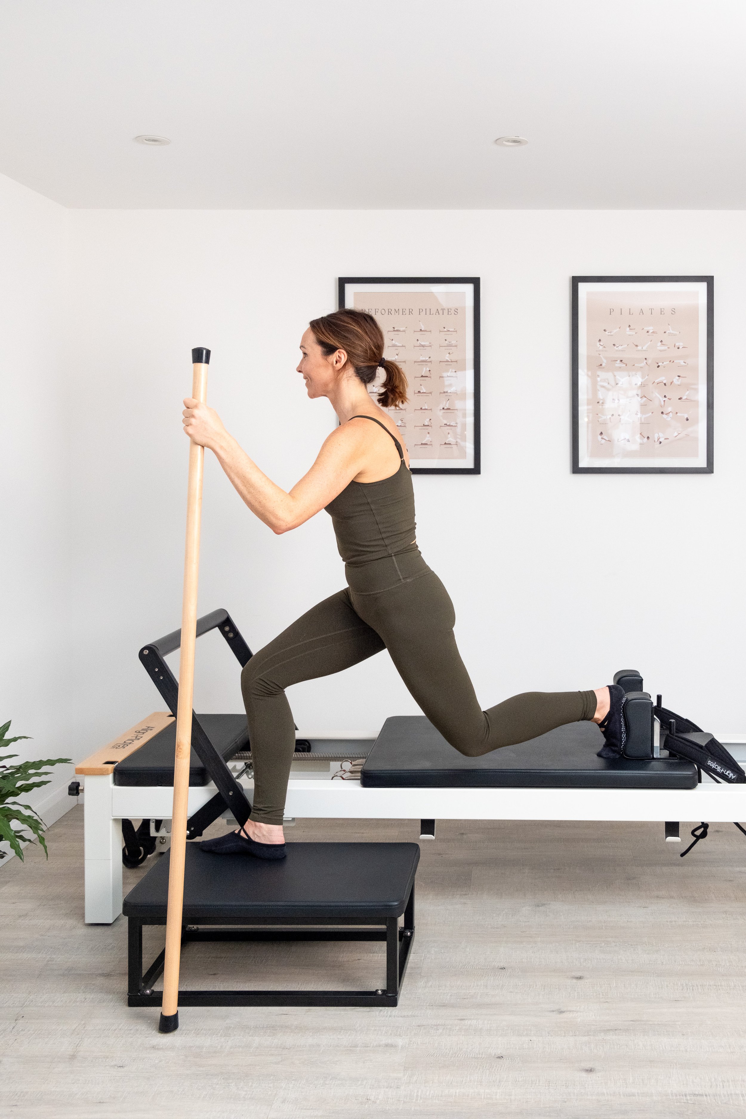 A woman performing a lunge exercise with a Pilates ring on a reformer machine in a Pilates studio.