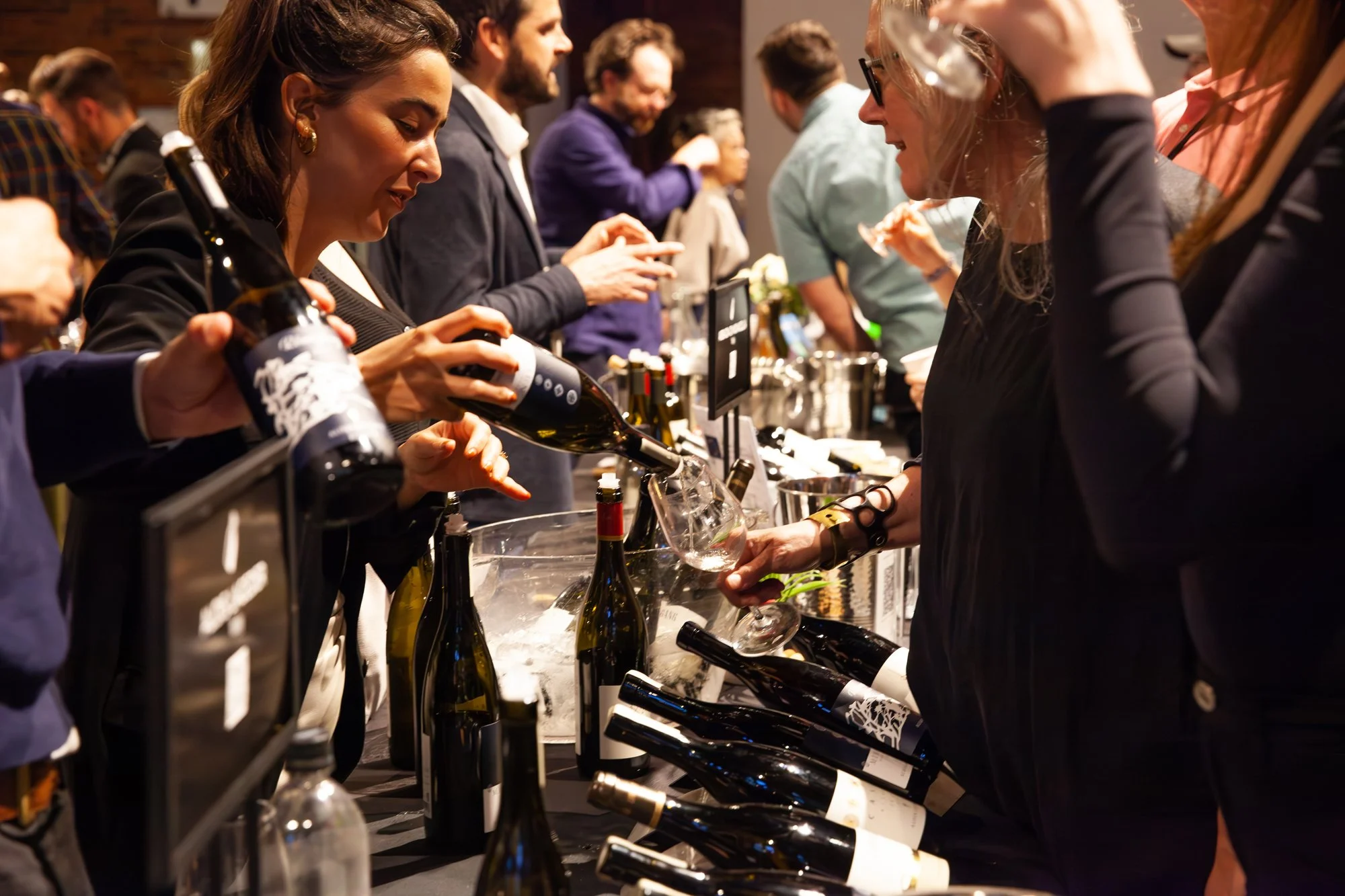 People sampling wine at a wine tasting event with bottles and glasses on a table at Top Drop Wine Festival in Vancouver