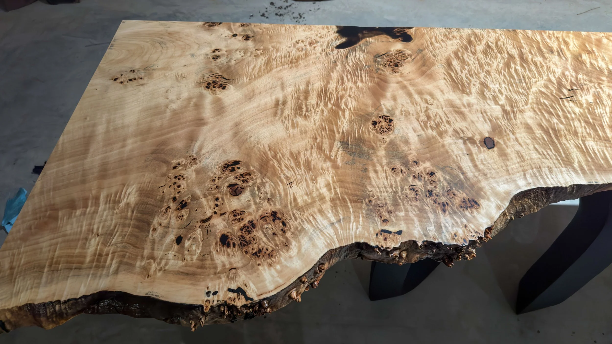 A polished wooden table with natural edges and unique grain patterns, featuring knots and irregularities.