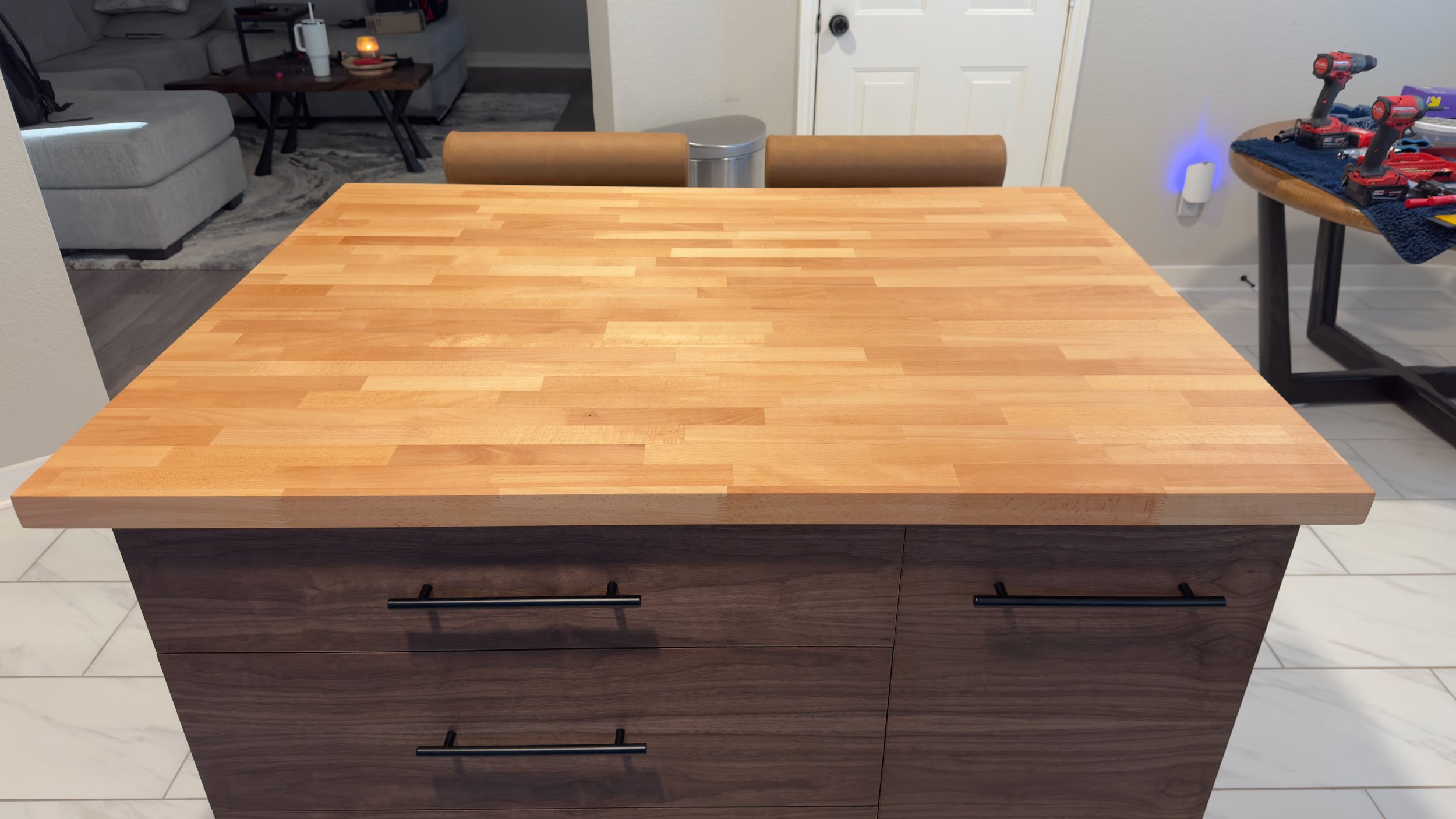 A wooden kitchen island with a butcher block top and dark wood drawers with black handles, situated on a tiled floor in a kitchen.