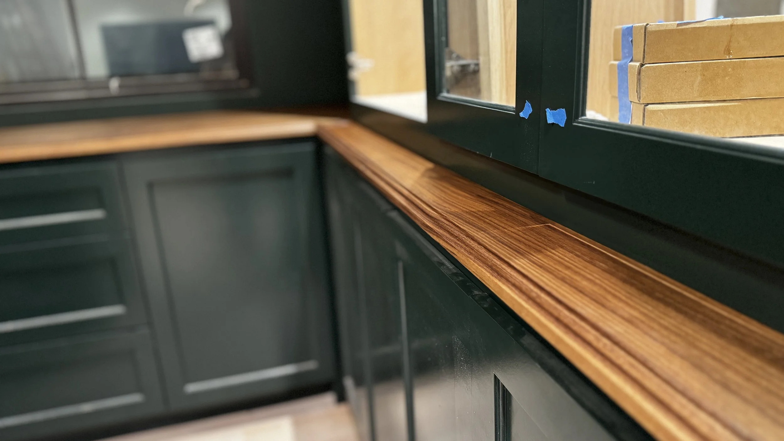 Long, narrow solid walnut countertop handcrafted and installed beneath dark green glass-front cabinets in a Fort Worth custom home.