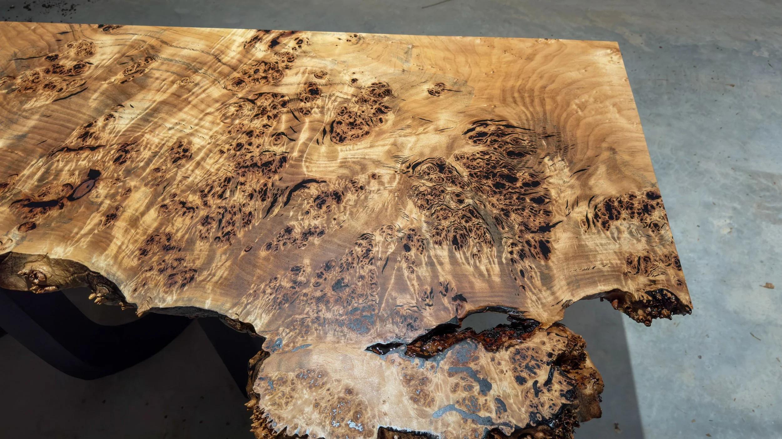 A wooden table with a natural, uneven edge and intricate grain patterns, showing a mix of light and dark wood tones.