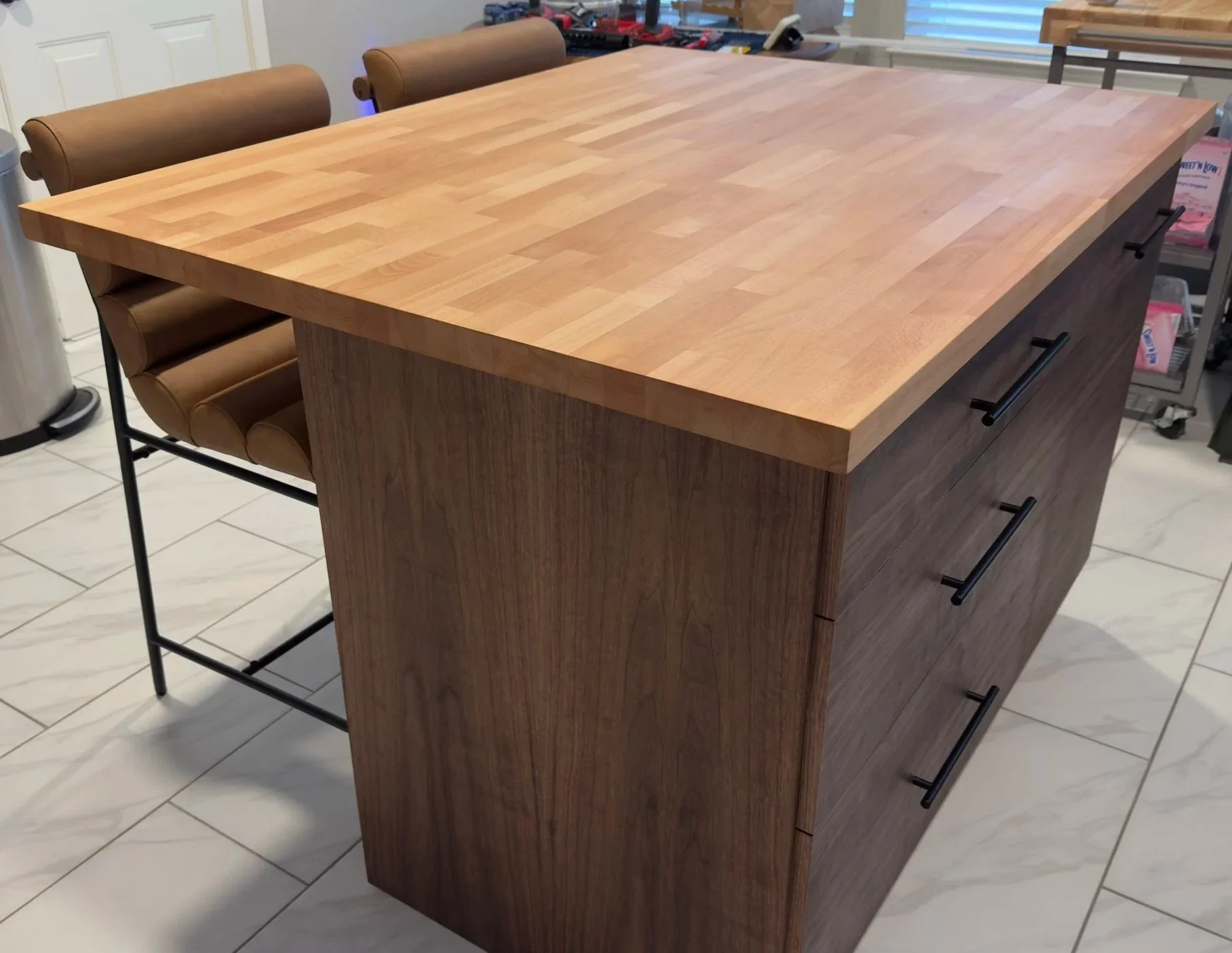 Custom made walnut kitchen island with large drawers and a pull out trash can. The island has a beech wood butcher block countertop and is paired with leather bar stools.