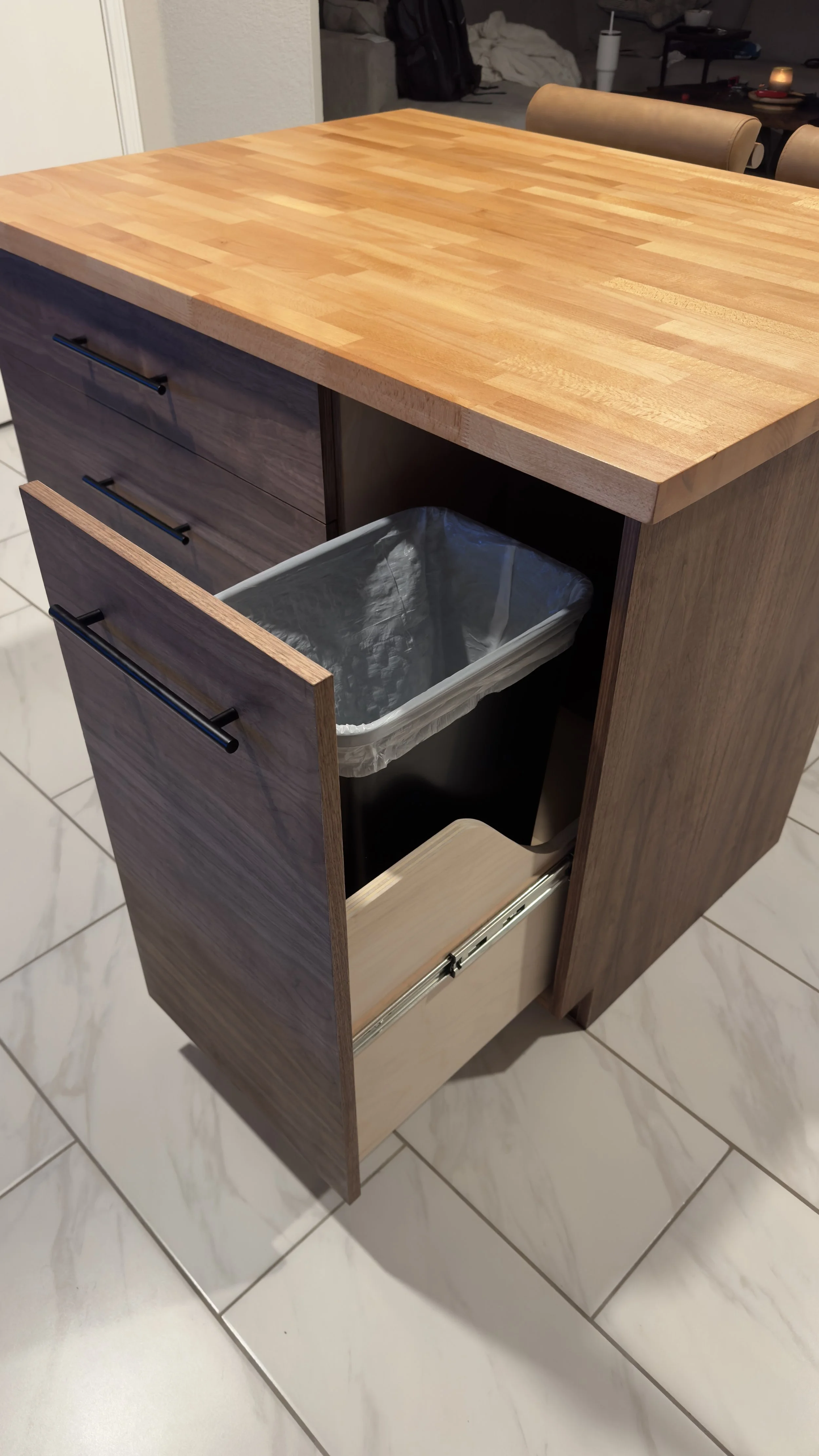 Open kitchen drawer with trash can inside, located under a wooden kitchen counter.