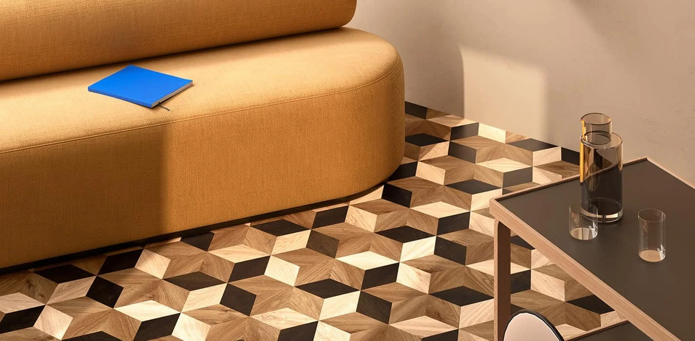 Sofá beige con cuaderno azul sobre él, mesa con jarrón y vasos de vidrio, suelo de patrón geométrico de madera y negro.