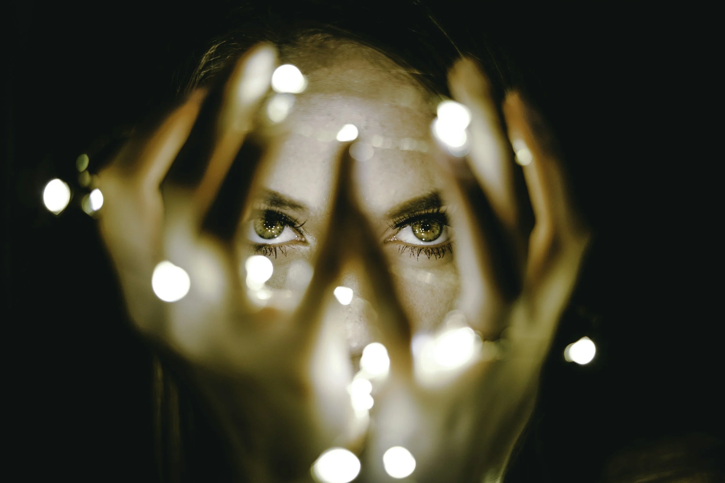A woman looking through a circular opening surrounded by bright bokeh lights, emphasizing her expressive eyes.