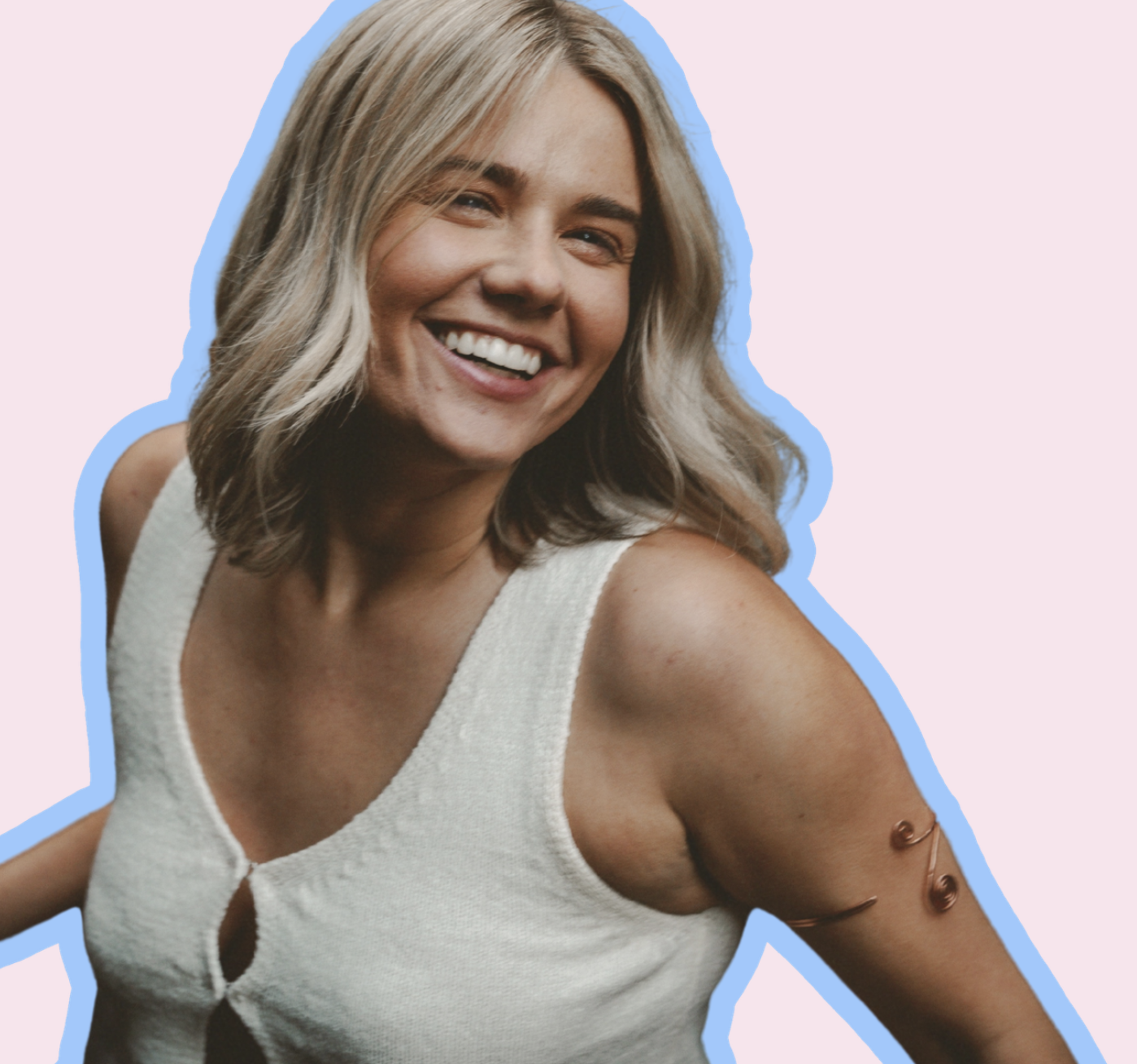 A smiling woman with blonde hair in a white sleeveless top, with a curly metallic temporary tattoo on her upper arm, against a pink background, outlined in blue.