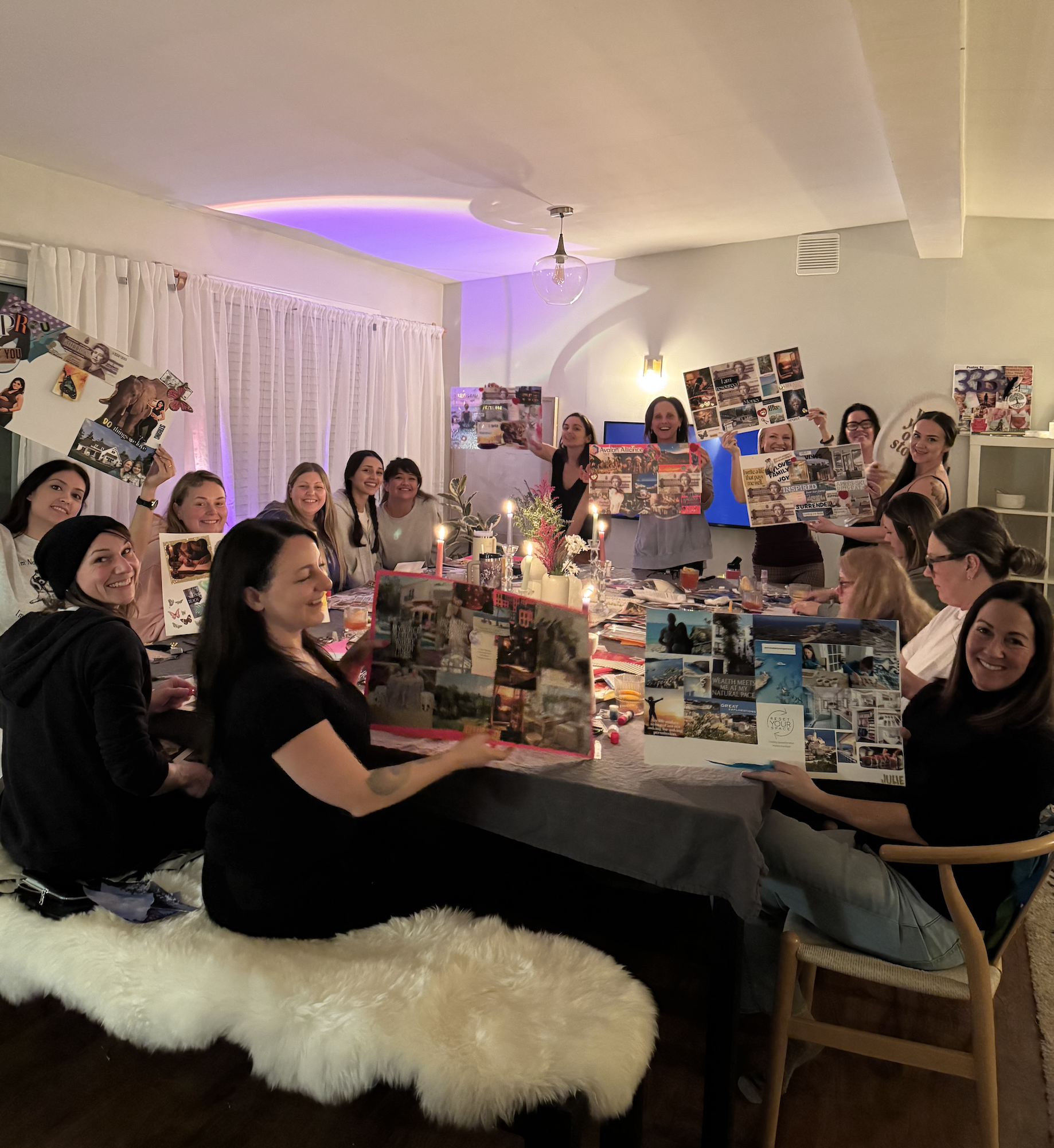 A group of women gathered around a dining table, celebrating with photo collages and candles in a cozy, decorated living room.
