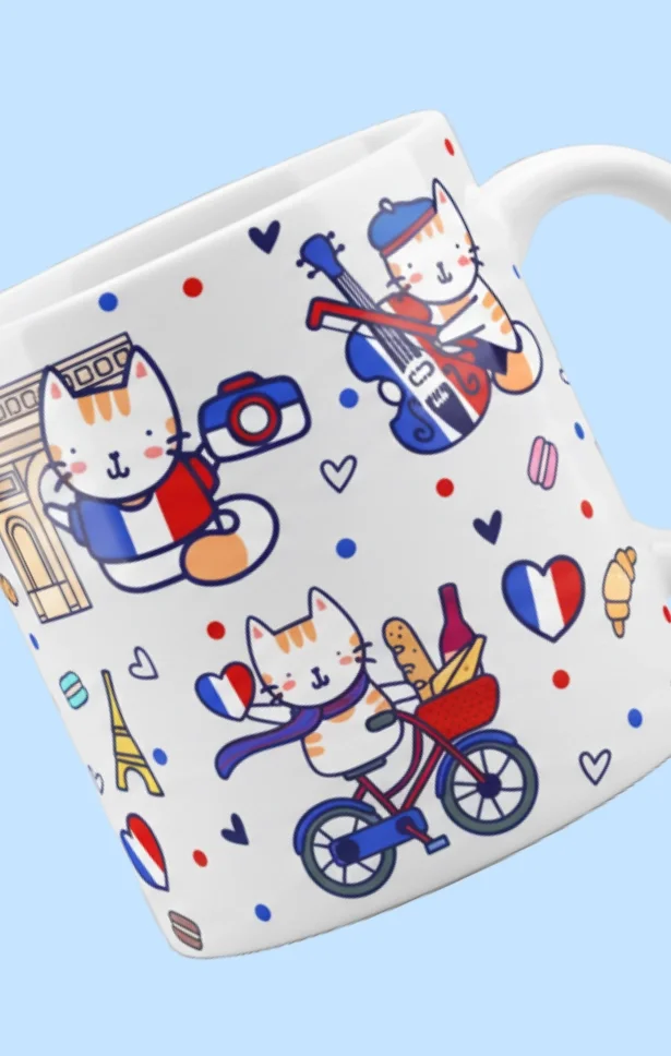 A white coffee mug with illustrations of cats engaging in French-themed activities, such as carrying a camera, playing guitar, and riding a bicycle, surrounded by small hearts, French flags, and food icons.