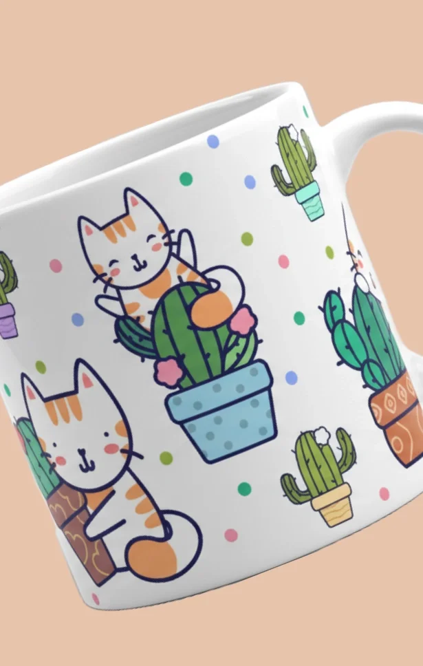 Close-up of a white ceramic mug with a colorful pattern of cartoon cats and cacti, set against a pink background.