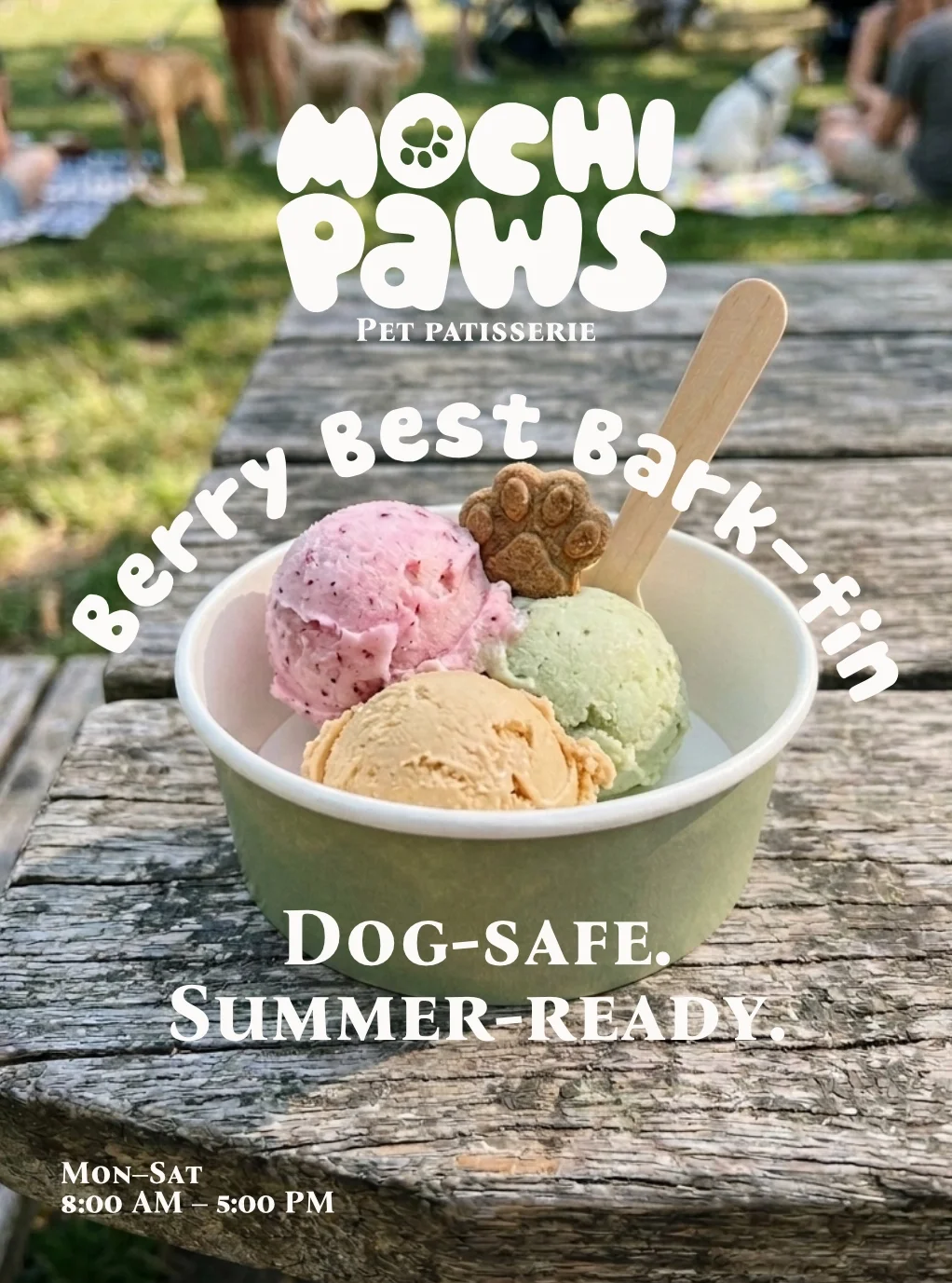 An ice cream cup with three scoops of ice cream in pink, green, and beige flavors on a rustic wooden surface with a background of outdoor seating and people. There is a wooden spoon and a small cookie on the ice cream. Overlaid text advertises Mochi Paws pet patisserie, highlighting berry flavor, dog-safe, and summer-ready treats, open Monday to Saturday from 8:00 AM to 5:00 PM.
