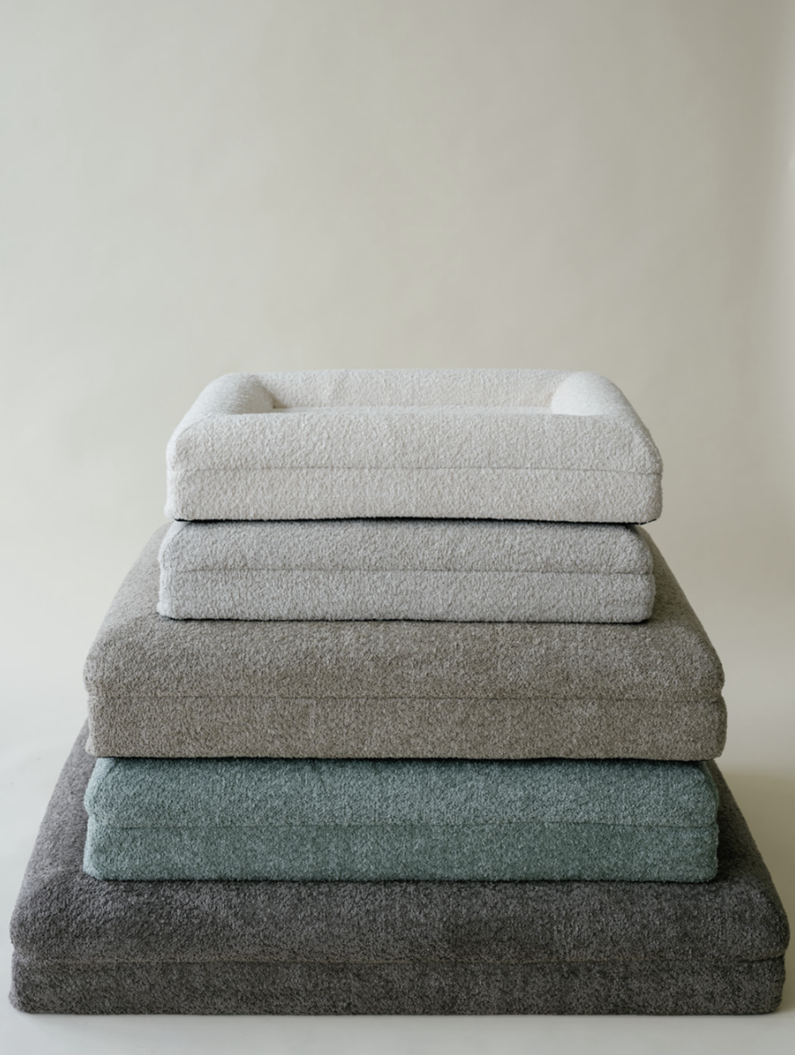 Stacked folded blankets in white, light gray, darker gray, teal, and charcoal colors.