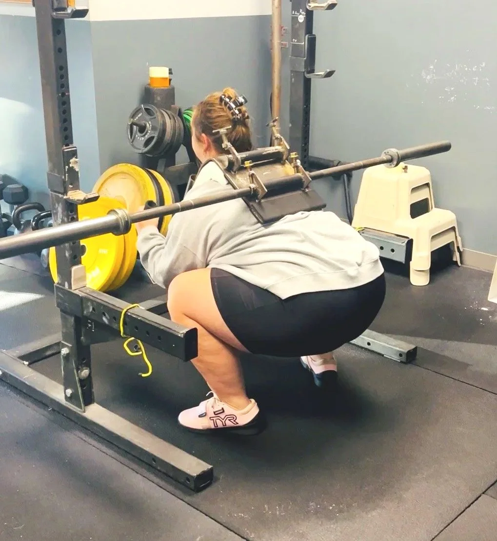 Woman performing a barbell squat using the Squat Baby attachment in a gym