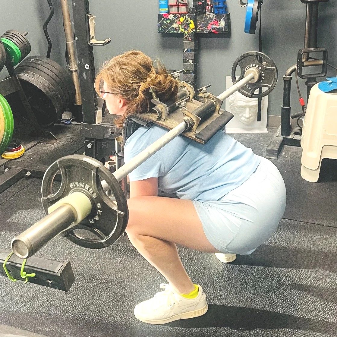 Woman squatting with a loaded barbell equipped with the Squat Baby attachment in a gym