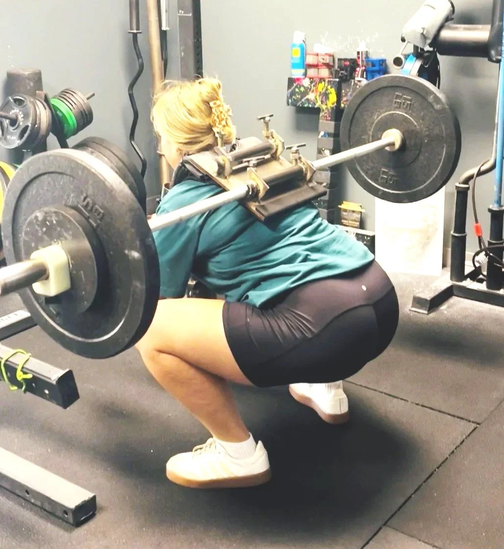 Woman performing a barbell squat with the Squat Baby attachment in a gym