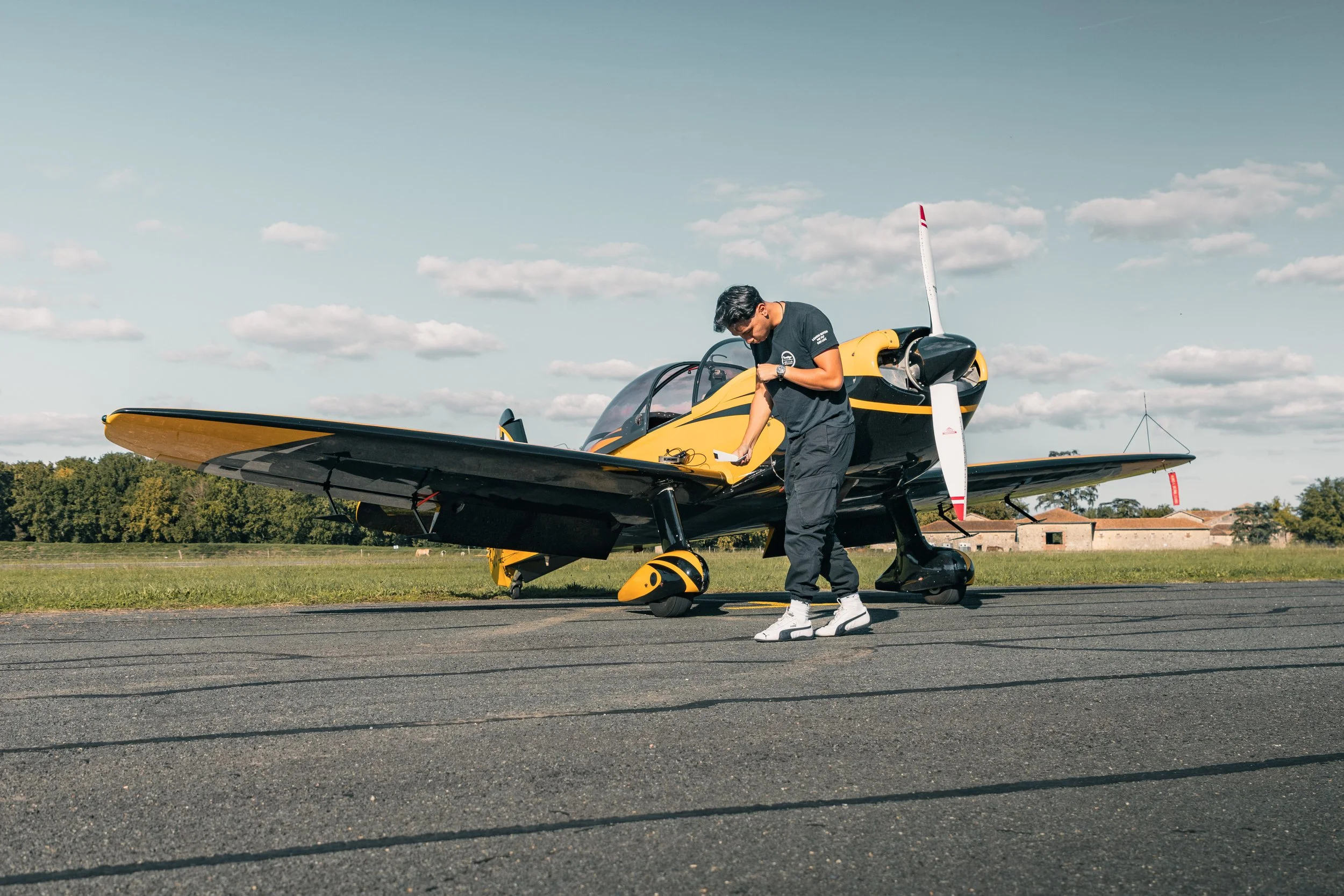 Un Pilote de voltige à côté d'un petit avion de Voltige jaune et noir CAP 10 sur une piste d'aviation aérodrome de Villeneuve sur Lot.