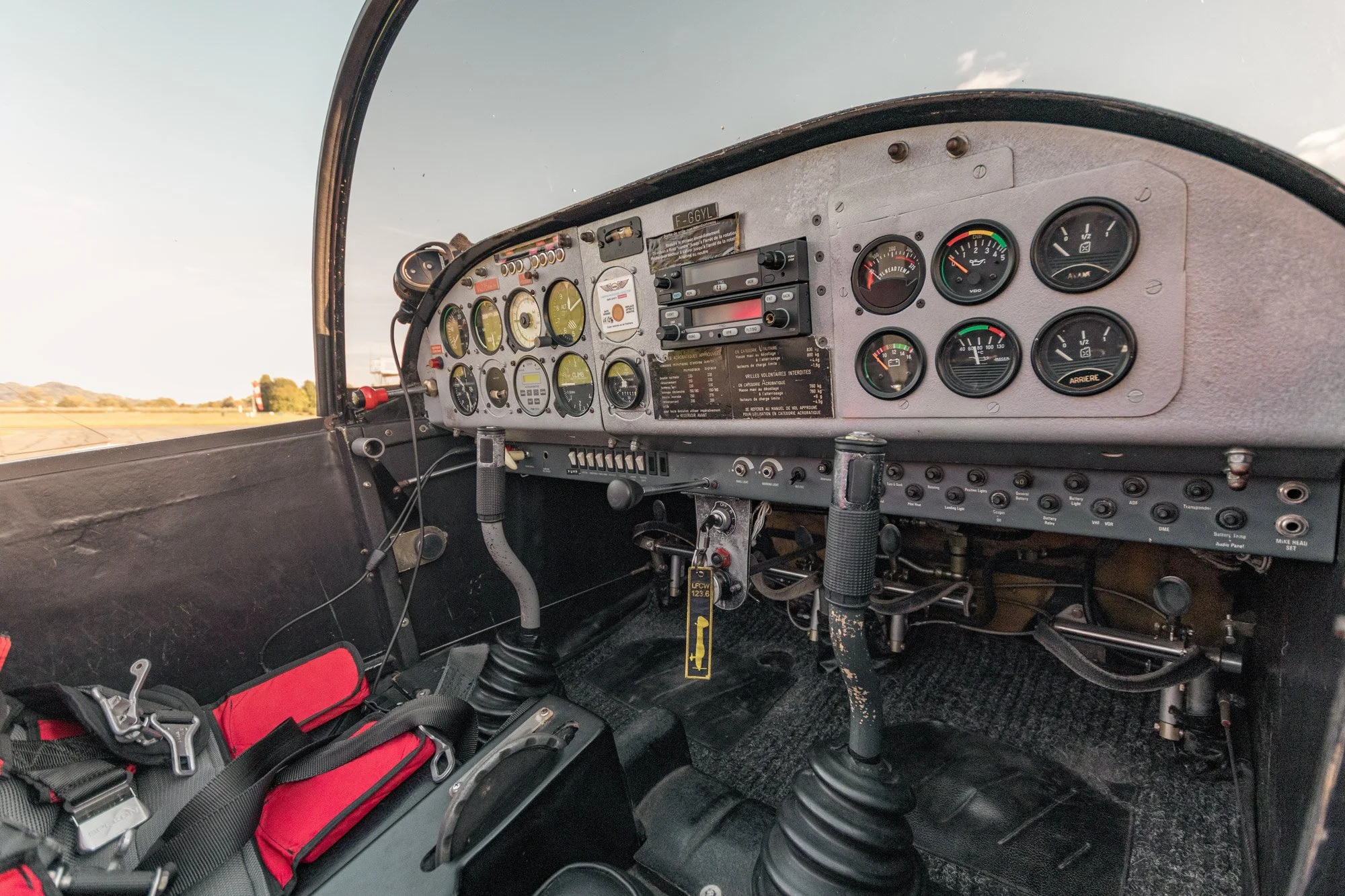 Intérieur d'une cabine d'avion avec tableau de bord contenant différents instruments de vol, leviers et sièges, vue vers l'avant avec un ciel clair visible à travers le pare-brise.
