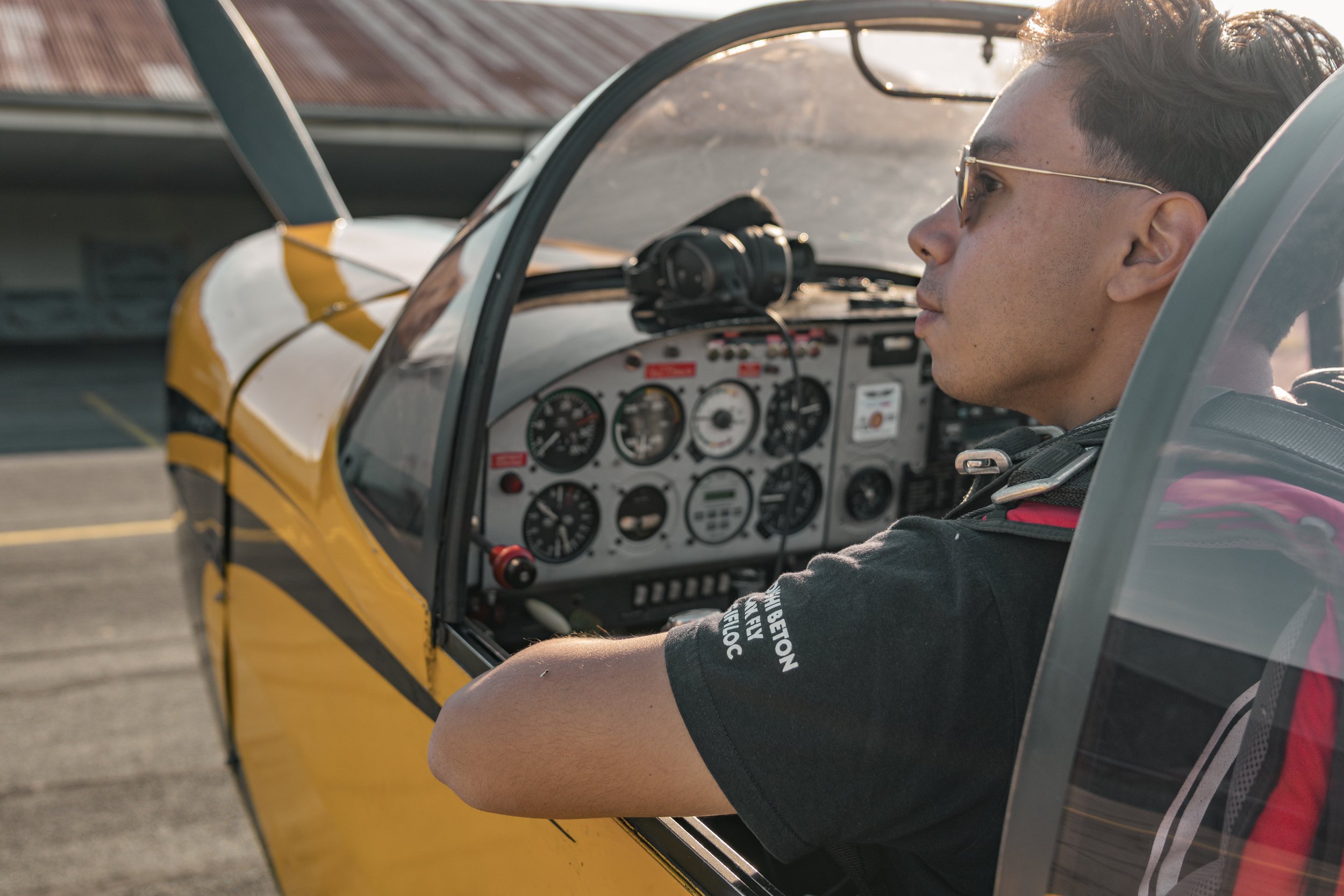 Jeune homme assis dans le cockpit d’un avion de voltige CAP10  avec tableau de bord rempli d’instruments, avec un harnais de sécurité, près d’un aéroport ou d’un terrain d’aviation de l'aérodrome de Villeneuve sur Lot.
