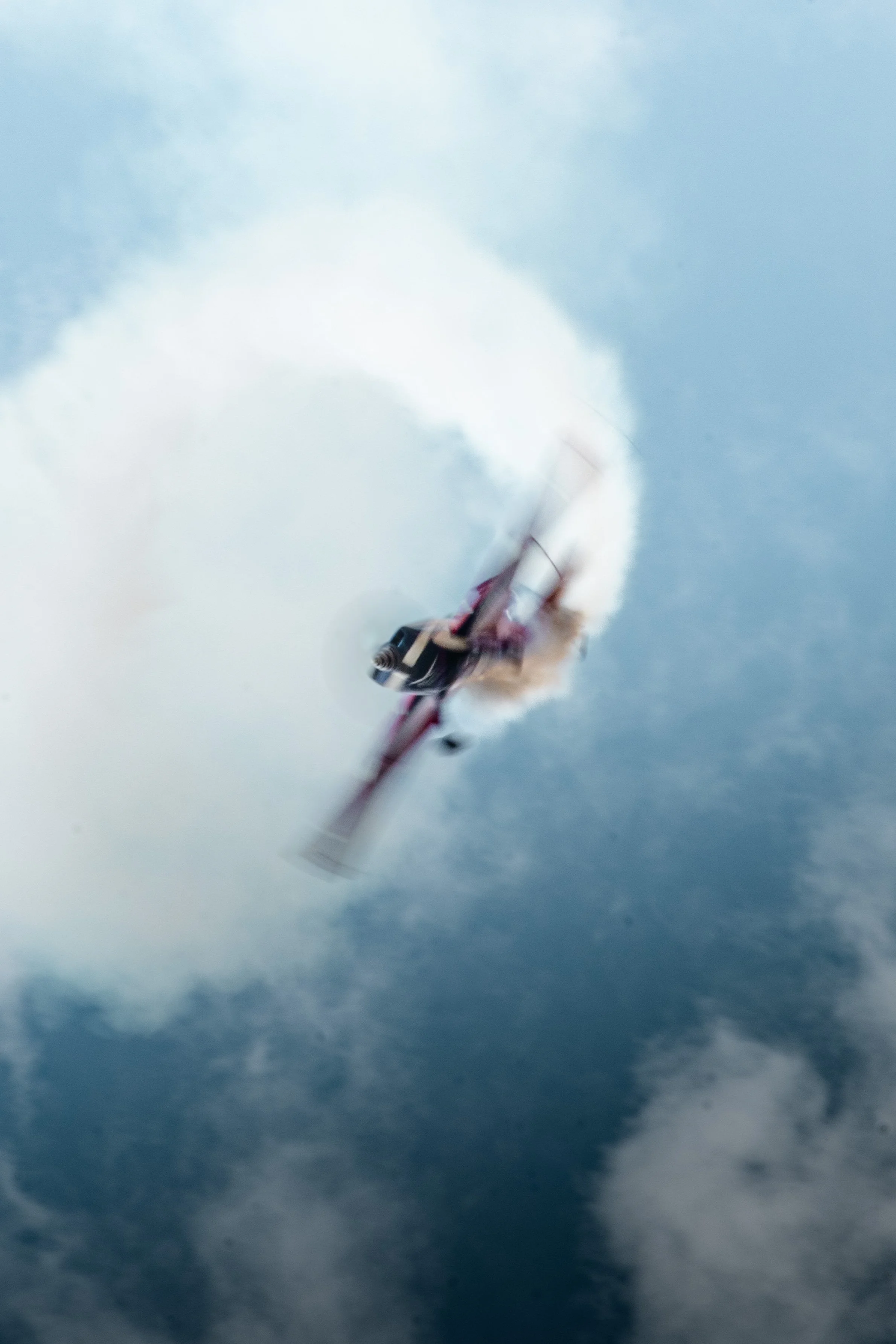 Un avion de Voltige Extra330 de l'équipe de voltige de l'armée de l'air et de l'espace effectuant un vol de voltige à grande vitesse, laissant une traînée de vapeur derrière lui dans le ciel nuageux.