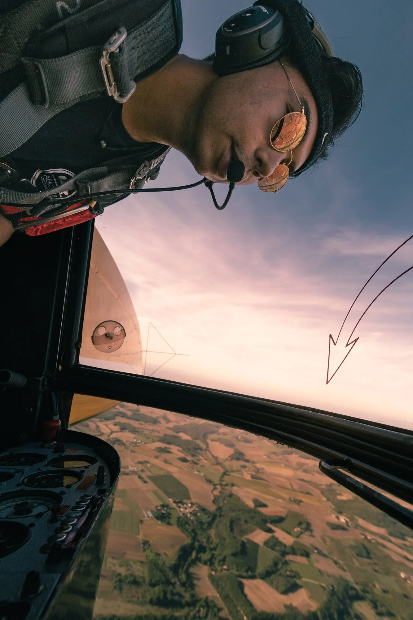 Pilote d'avion en vol avec vue sur le paysage agricole en dessous, ciel du soir avec traces de condensation et un éclair dans le ciel.