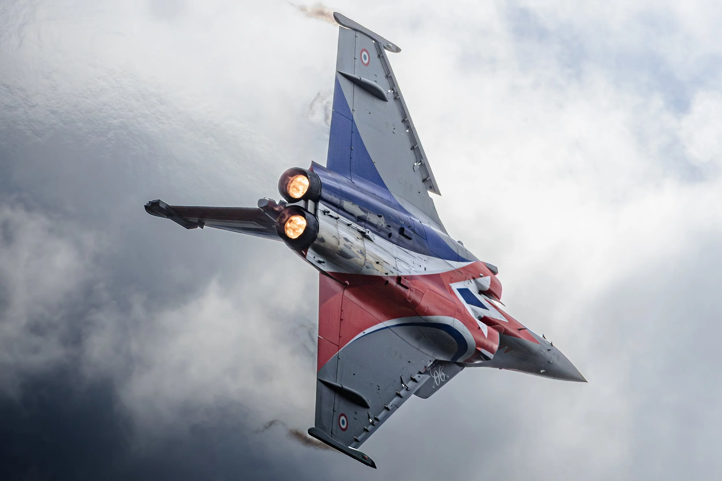 Un avion de chasse Français Rafale solo display RSD en vol dans un ciel nuageux, avec des étoiles françaises sur ses ailes et ses fuselages.