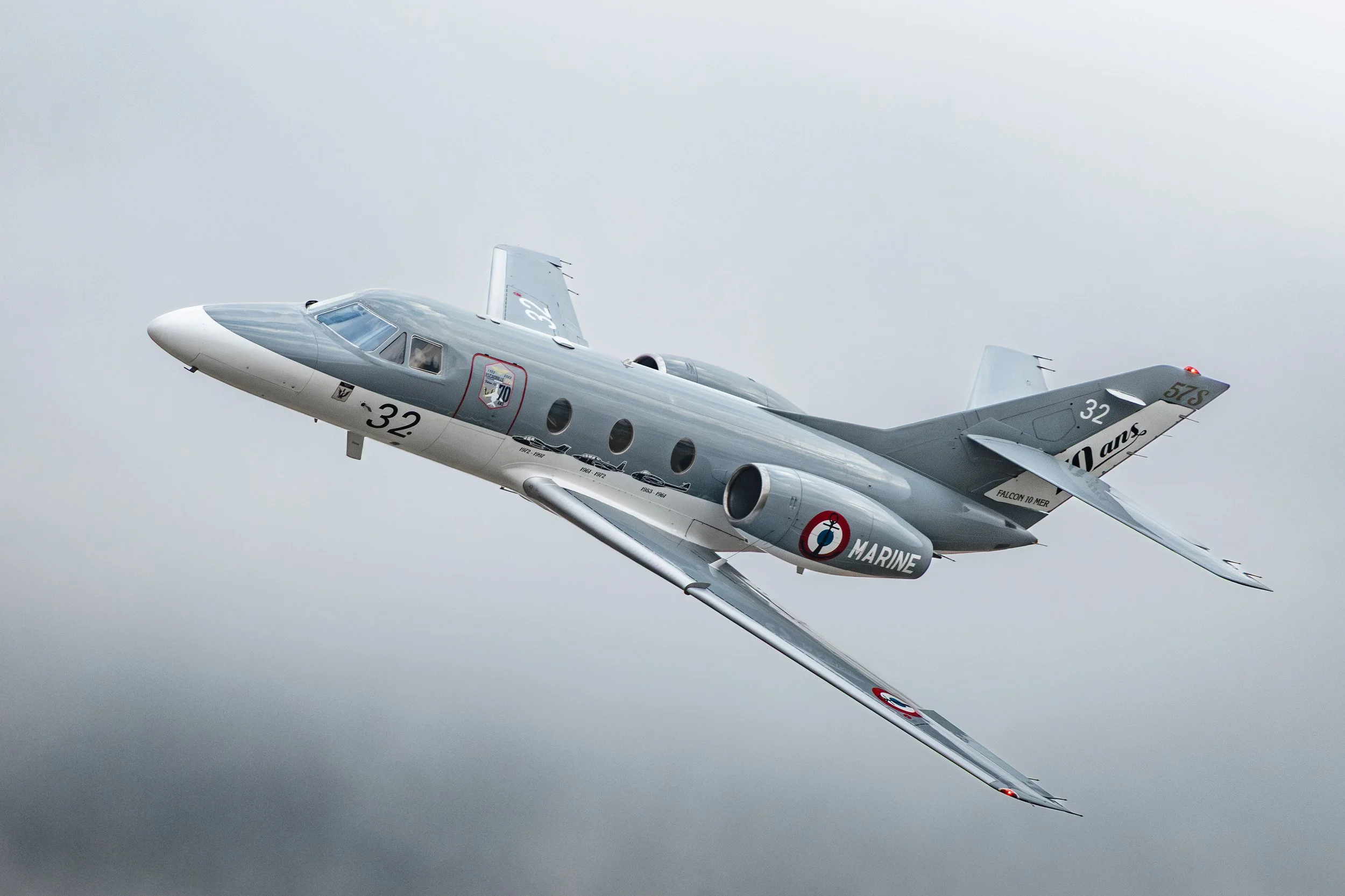 Un avion de chasse en vol, gris et blanc avec des inscriptions de la Marine française, en plan rapproché contre un ciel gris.