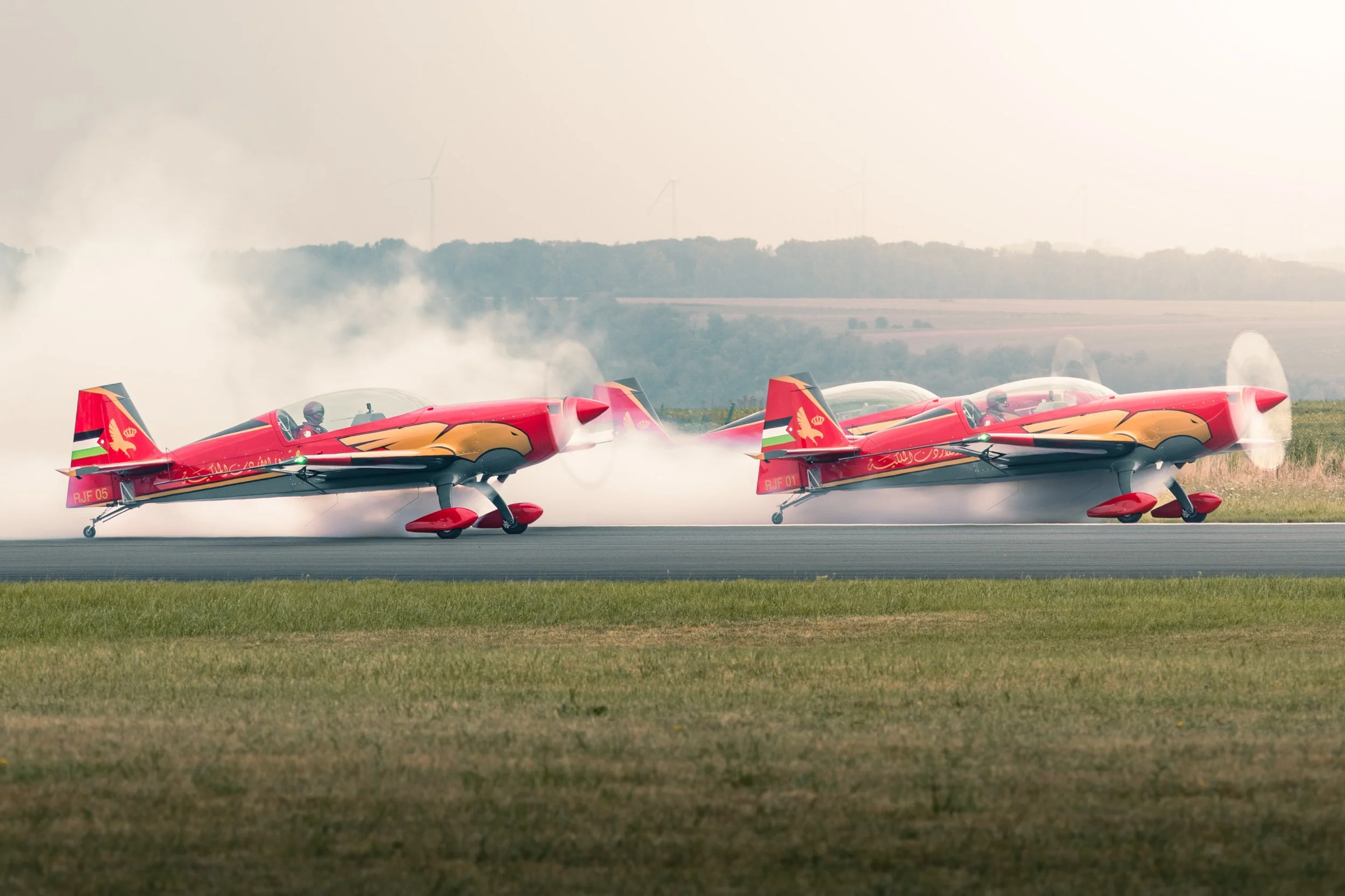 Deux avions de voltige en train de réaliser un atterrissage ou un décollage sur une piste, avec de la fumée ou de la vapeur autour d'eux.