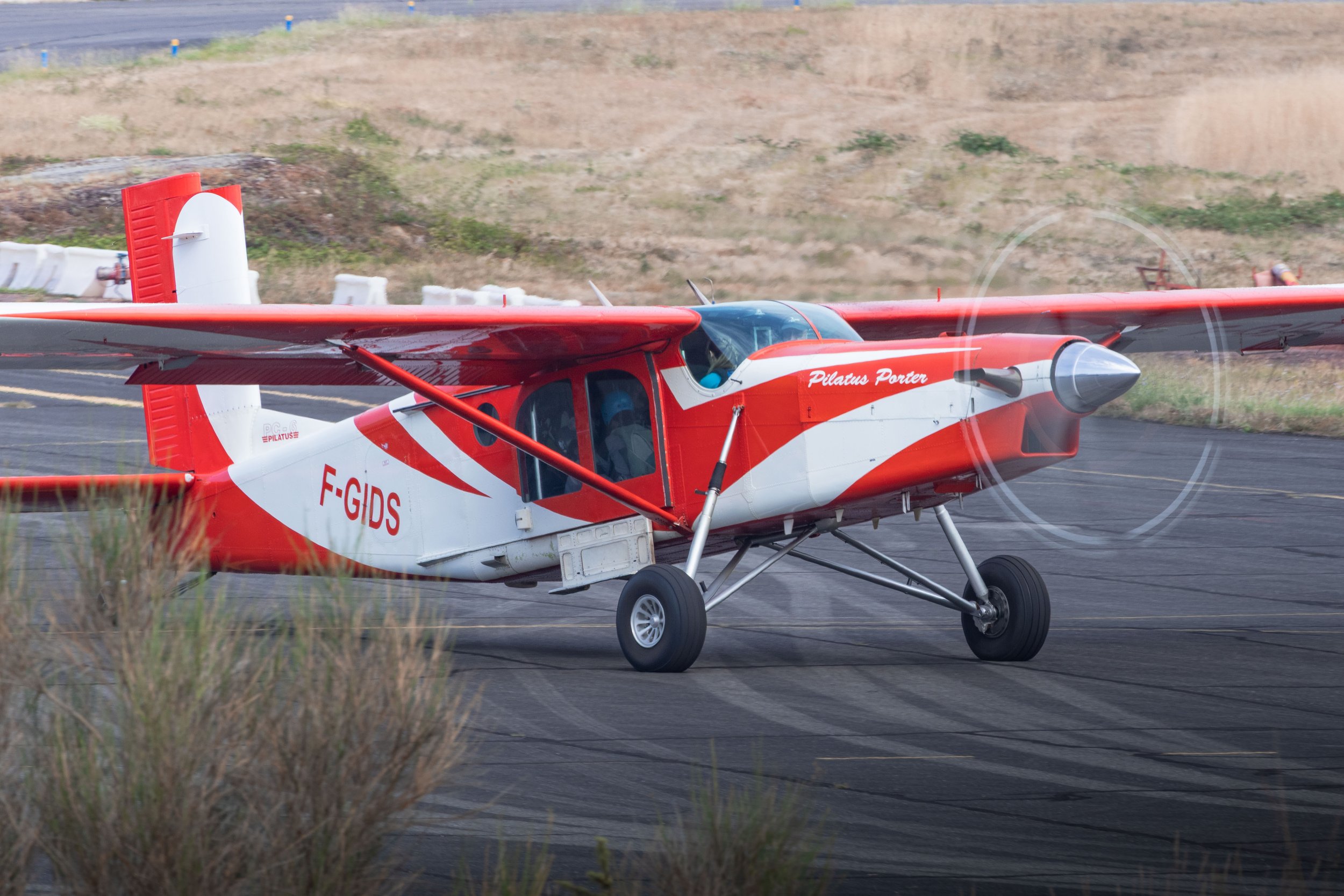 Un avion de parachutisme rouge et blanc du Club de parachutisme de Cahors Lalbenque, portant le nom 'Pilatus Porter' et le code 'F-GIDS', roule sur la piste lors d'un atterrissage.
