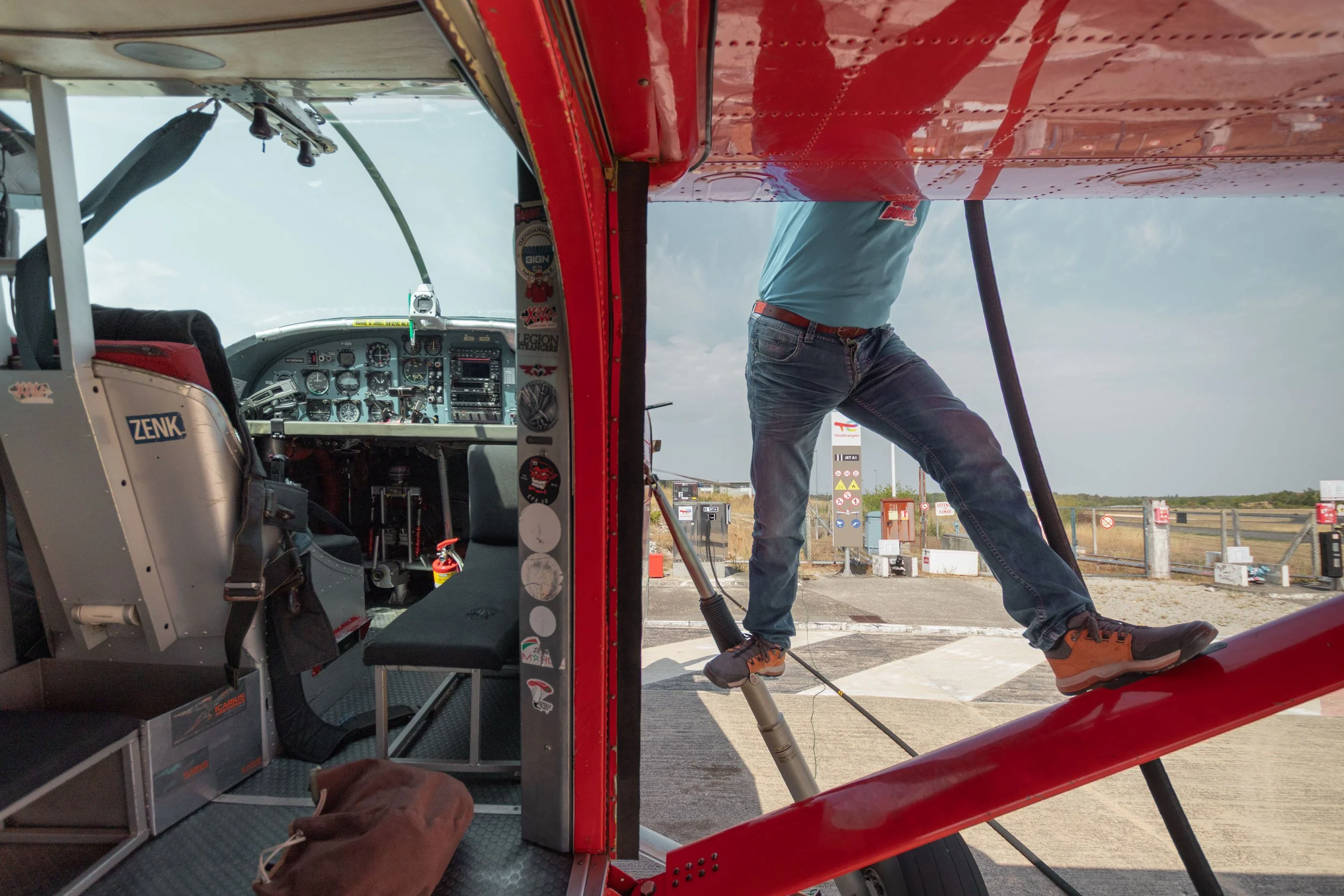Intérieur d'un avion Pilatus avec tableau de bord et siège, avec une personne dehors en train de faire le plein ou d'inspecter l'aéronef, dans une station-service en plein air.