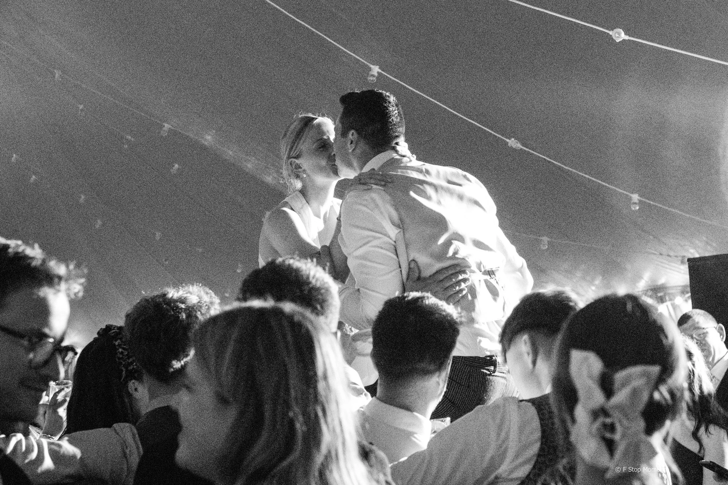 Couple celebrating on guests’ shoulders at a wedding — black and white documentary photography