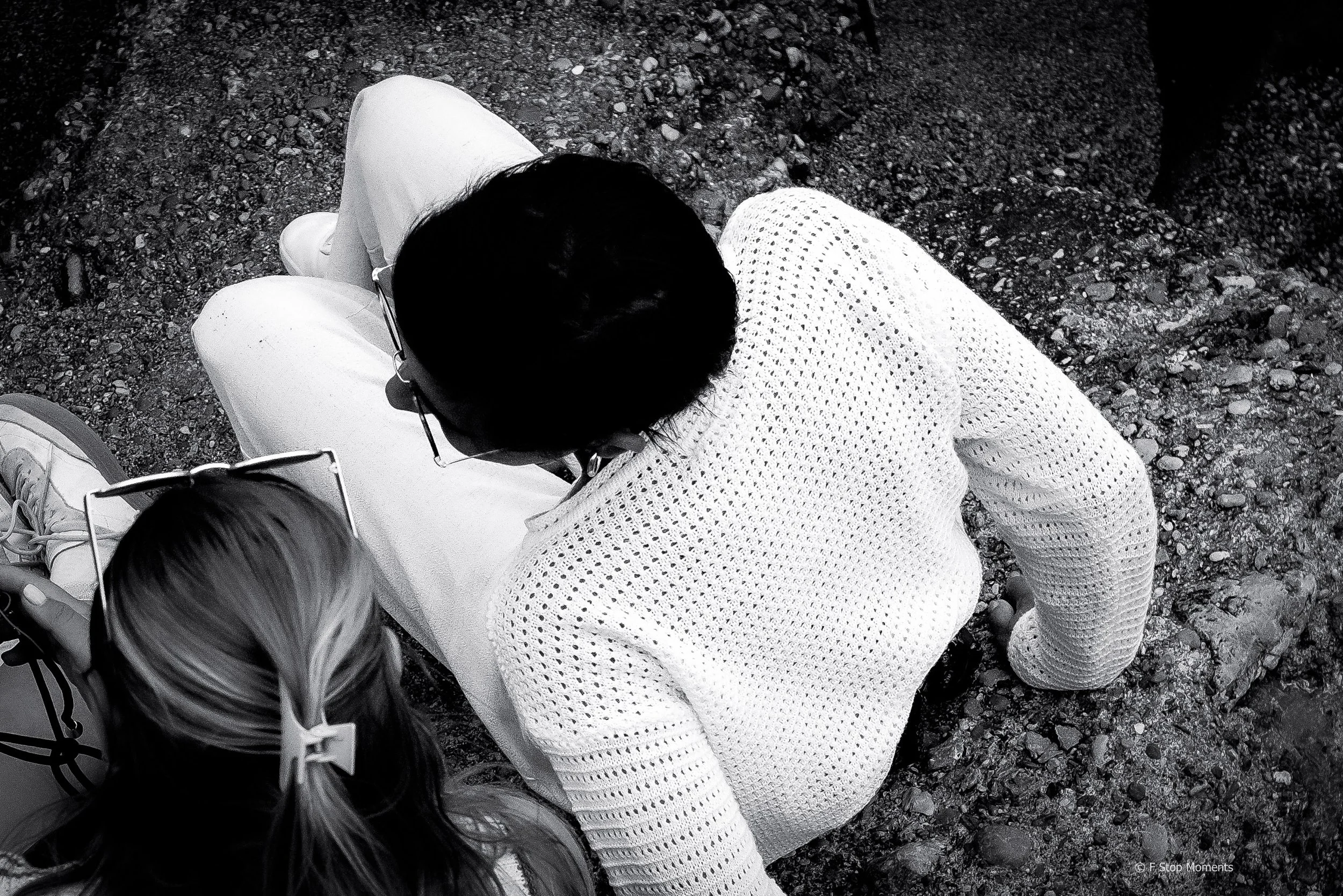Black and white image of a couple sitting on a rocky beach after a wedding.
