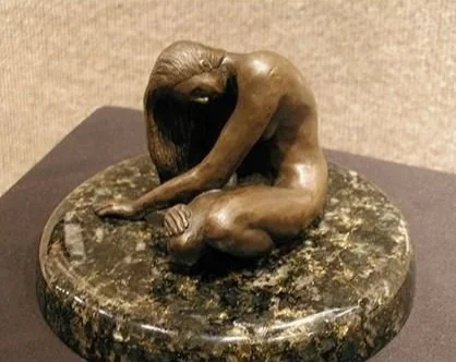 A bronze sculpture of a person sitting with their head down and arm covering their face, placed on a round stone or marble base.