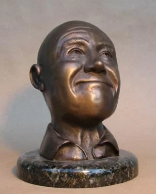Bronze bust sculpture of a smiling young boy with a round face and short hair, mounted on a round stone base.
