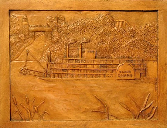 Bas-relief plaque depicting a ship named 'Island Queen' with trees and cliffs in the background.