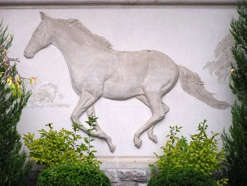 White horse wall sculpture with green plants in front.