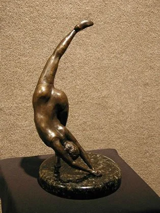 Bronze sculpture of a person in a handstand pose, on a round base.