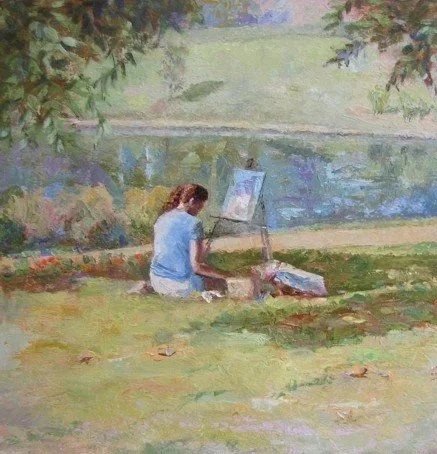 A woman sitting on the grass painting near a lake.