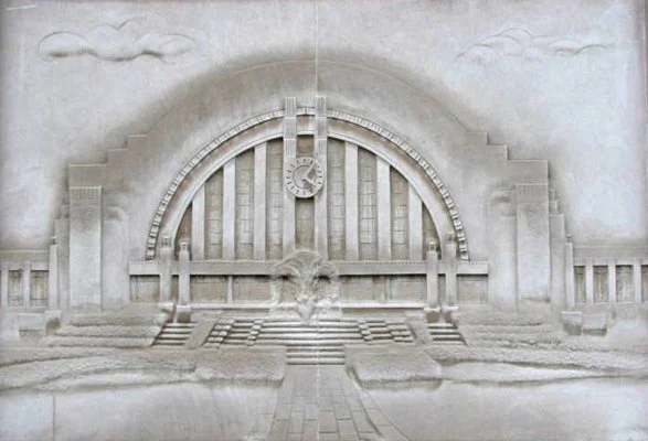 Sand sculpture of a large clock tower with a prominent archway and steps, flanked by stylized buildings and clouds.