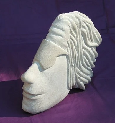 Sculpture of a face with a headphone-like object over the eyes, made of white material, with stylized hair or head details, placed against a dark purple background.