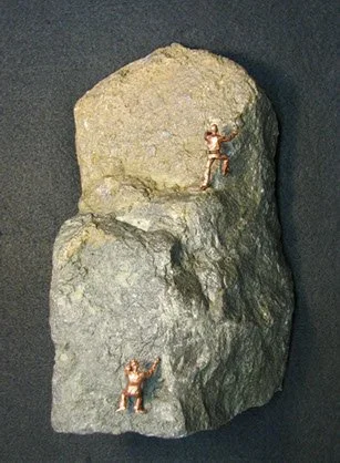 Two tiny humanoid figurines on a large gray and beige rock.