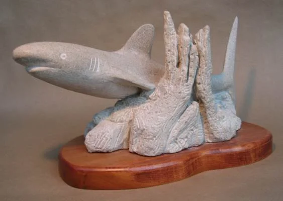 Carved stone sculpture of a shark on a wooden base.