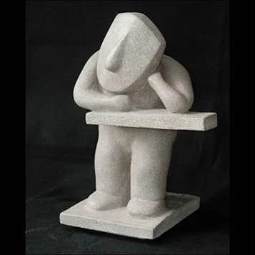 Statue of a person wearing a hat, leaning on a table with one hand, holding a pen with the other, made of light-colored stone or material.