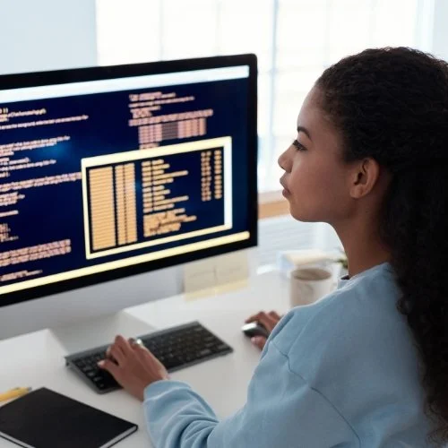 Woman working on a computer with a programming or code screen open.