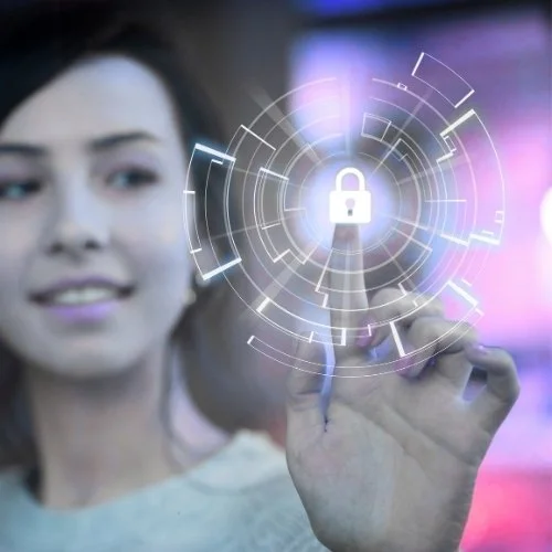 A woman in a blurry tech background touches a virtual screen displaying a glowing padlock and futuristic digital security graphics.