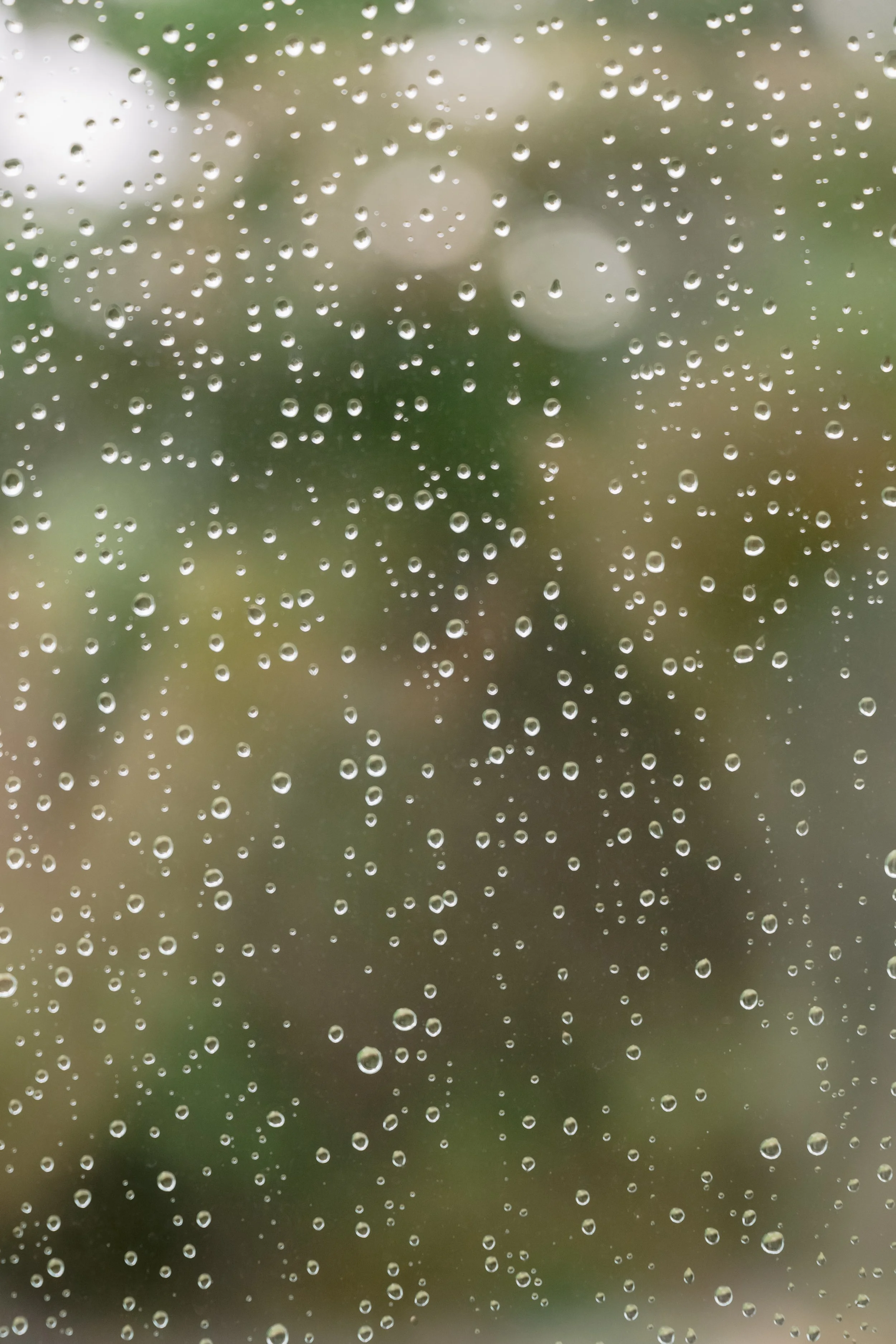Raindrops on a glass window with a blurred outdoor scene in the background.