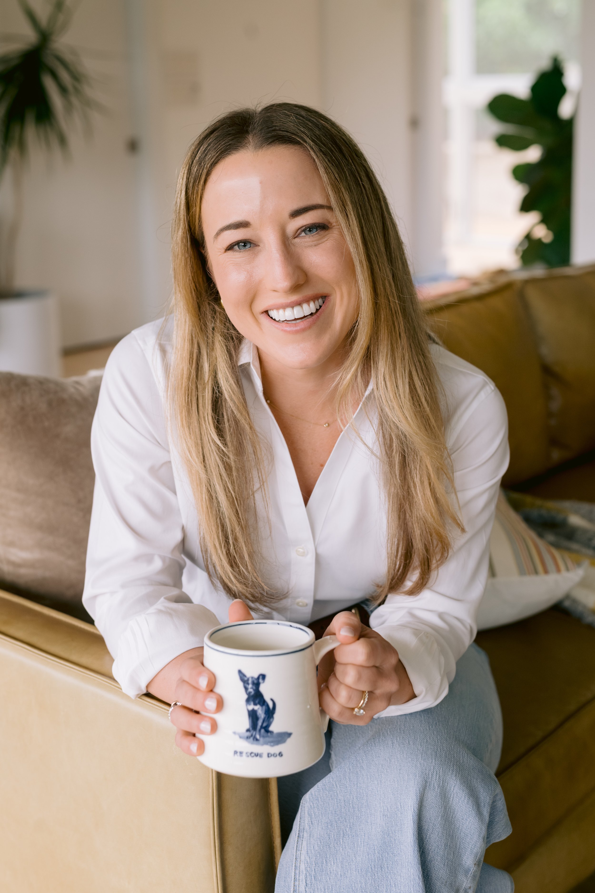Therapist sitting on a couch, holding a coffee mug, leaning in and smiling